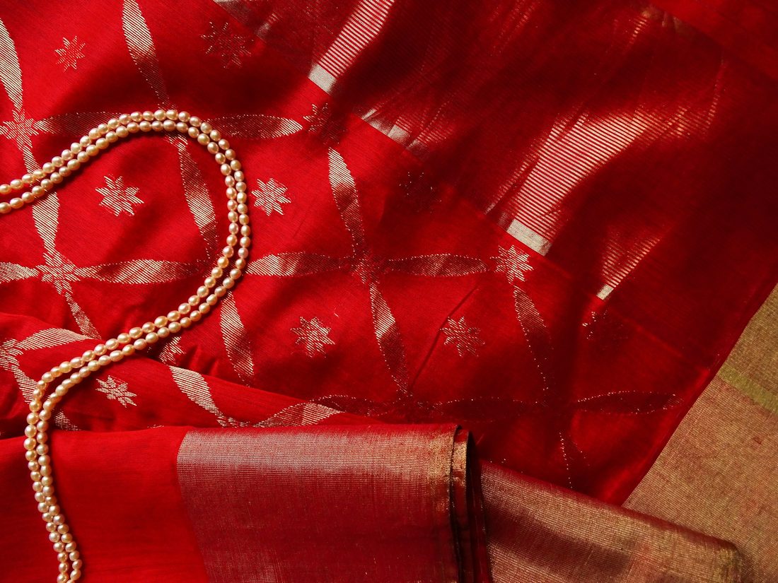 Red silk saree with silver zari lattice weave beside a string of pearls