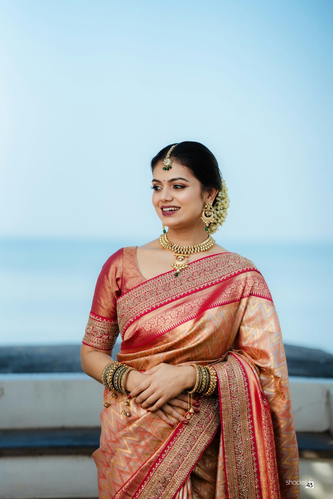 Bride in a cream and orange Kanchipuram silk saree with gold jewellery against a blue sky