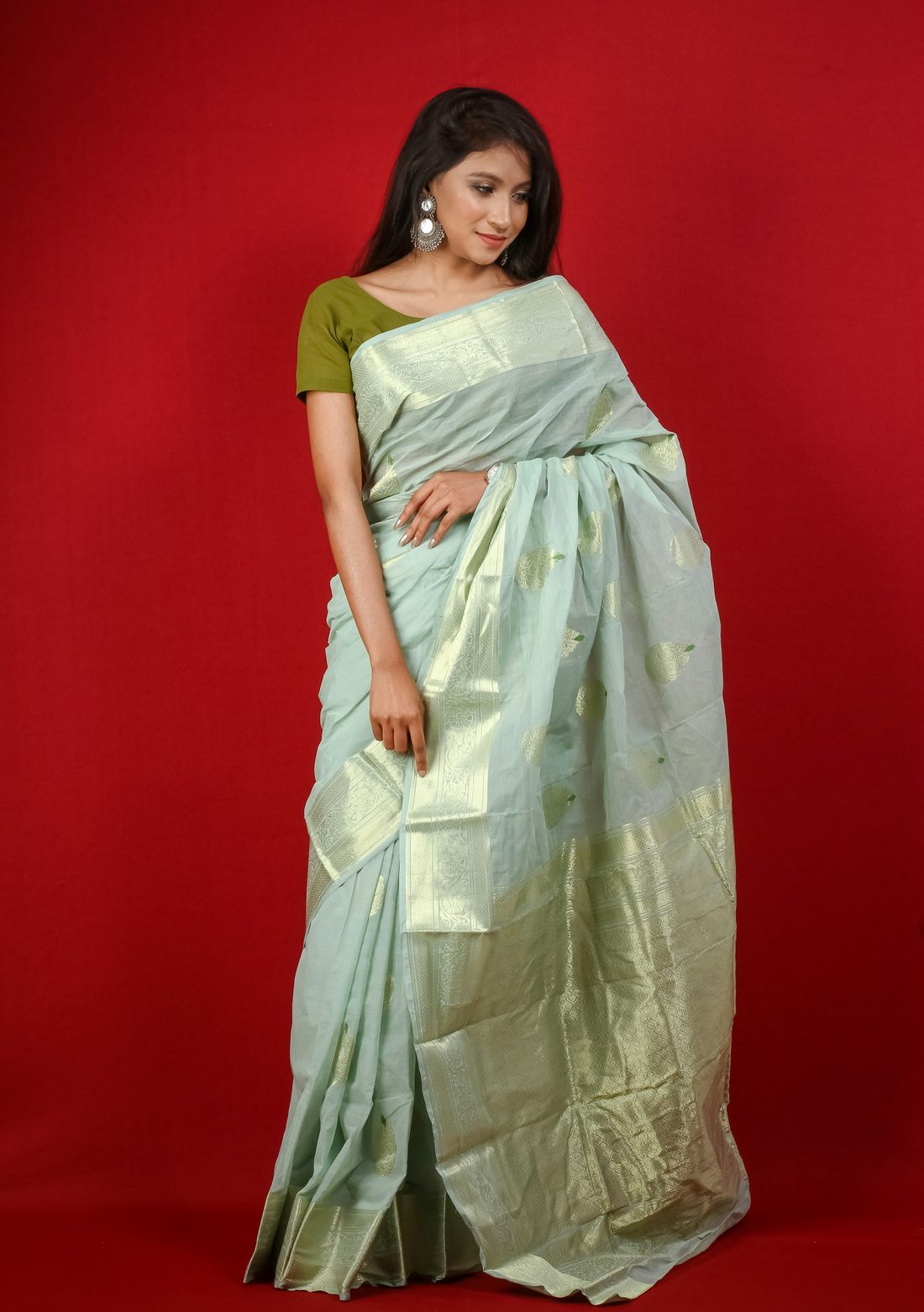Pale mint soft silk saree with a fine gold border, draped against a deep red wall