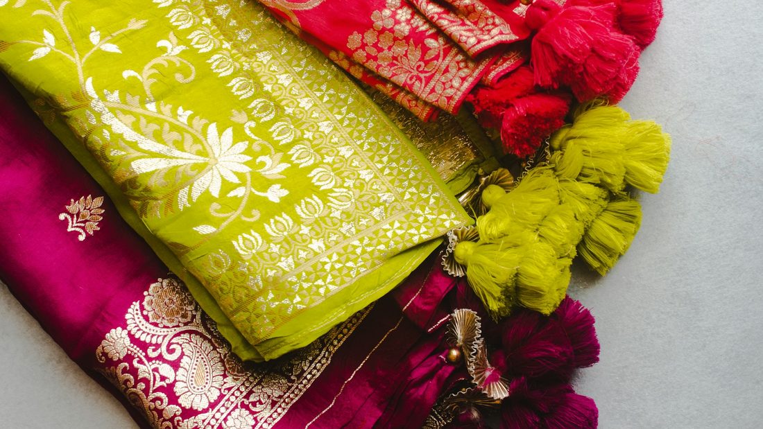 A stack of folded silk sarees in lime green and magenta with silk tassels
