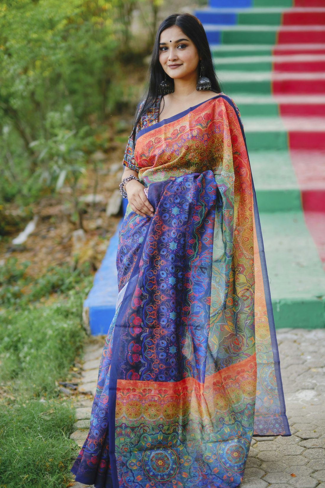 Woman in a blue printed saree with a colourful border, standing outdoors