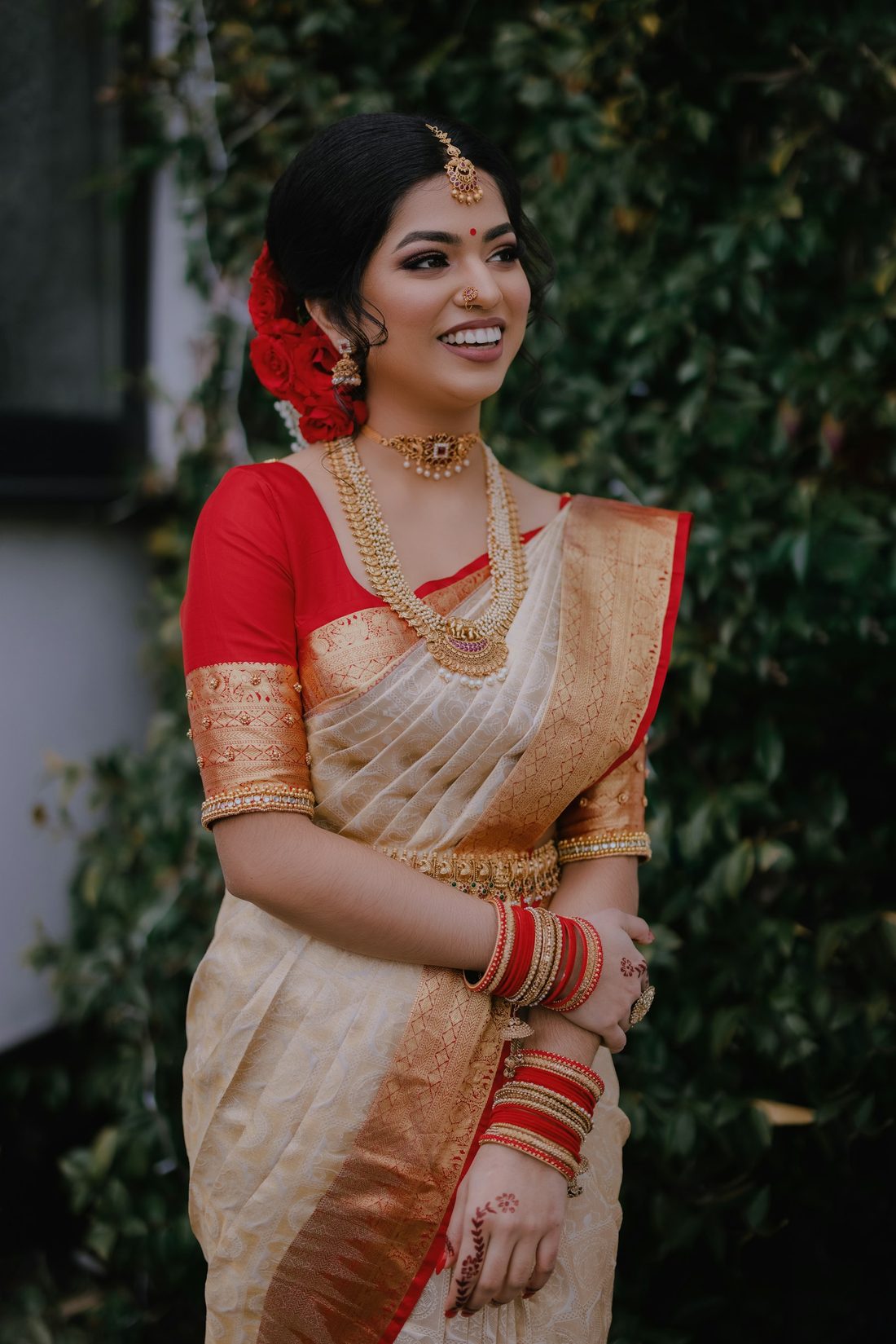 Bride in a cream Kanchipuram silk saree with red border and gold jewellery, smiling