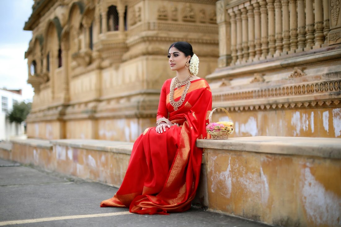 Woman in a red silk saree seated on the stone steps of an old temple